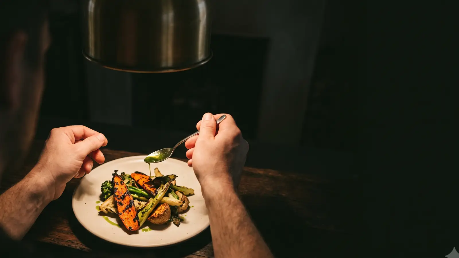 Hands finishing a plate at the pass, brass lamp overhead